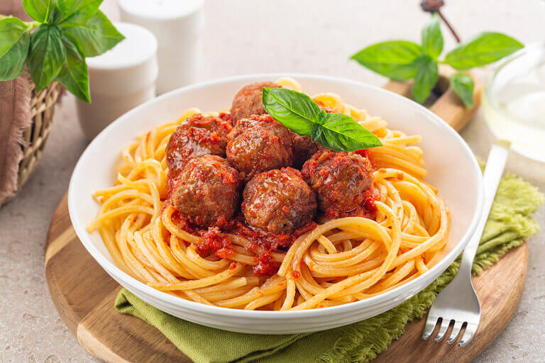 A heaping amount of spaghetti is topped with meatballs and a red sauce on a brown plate, with a knife and fork to the right of the plate.