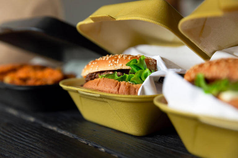 A row of three slightly-open to-go containers, two of which contain burgers.