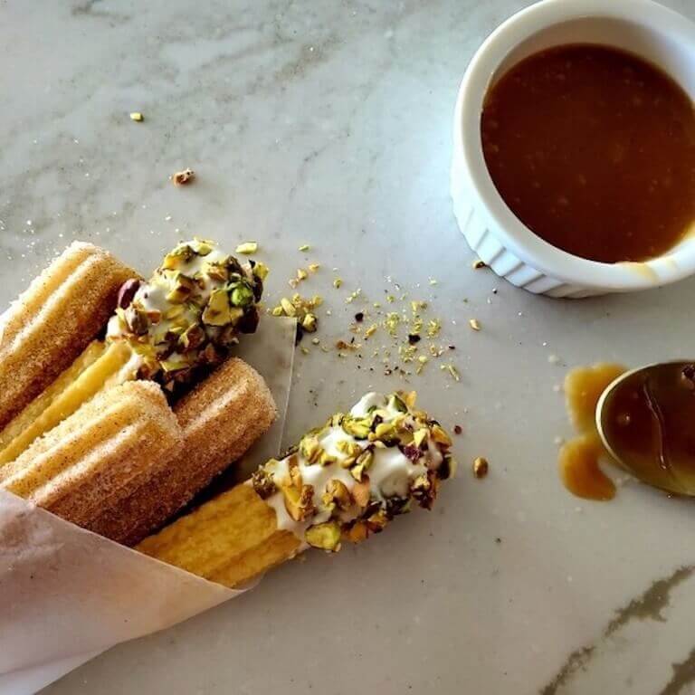 Churros arranged on a plate with a bowl of caramel sauce, set on a wooden surface.