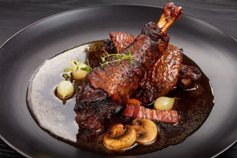 A leg of lamb sits in mushroom gravy on a black plate.