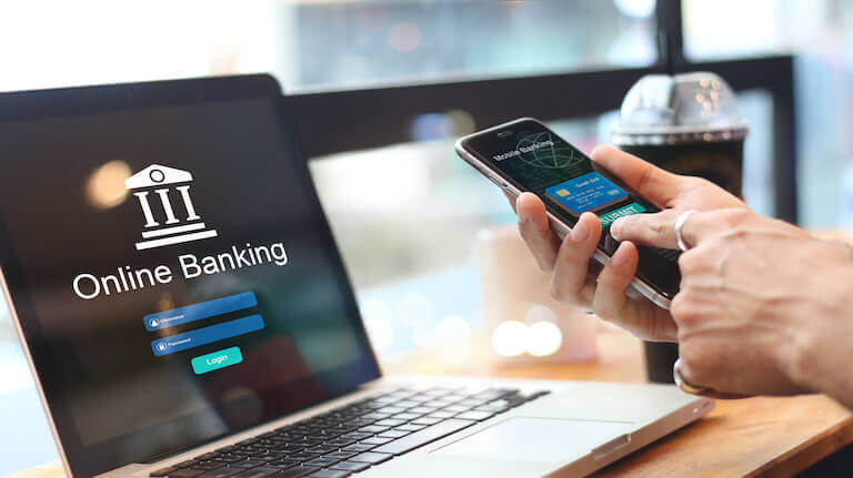 Close up of person using an online banking app on a smart phone while sitting in front of a computer