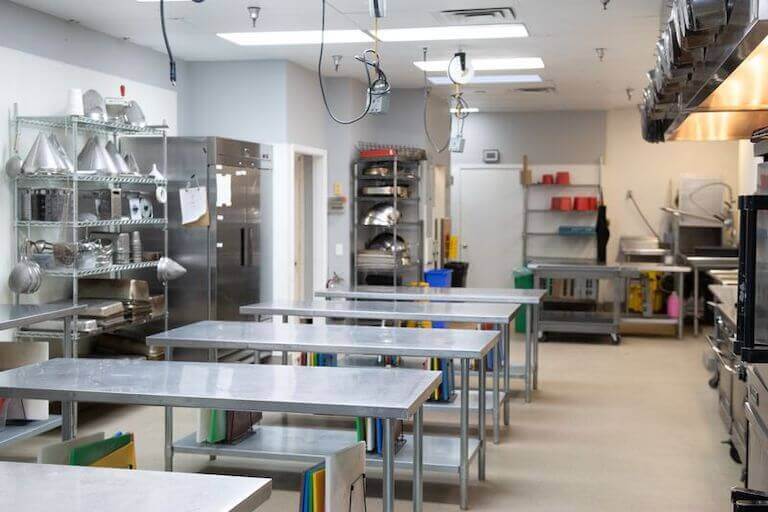 A culinary school kitchen with stainless steel work stations surrounded by racks of cooking equipment.