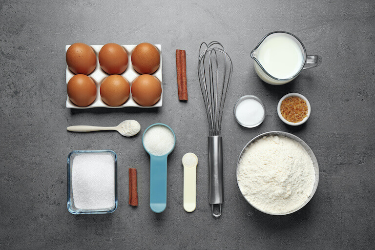 Ingredients to make muffins are laid out in mise en place, including eggs, flour, sugar, salt, and milk.
