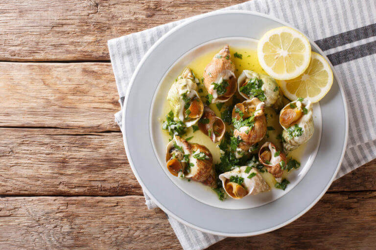 Nine escargots sit in a white wine and butter sauce on a white plate.