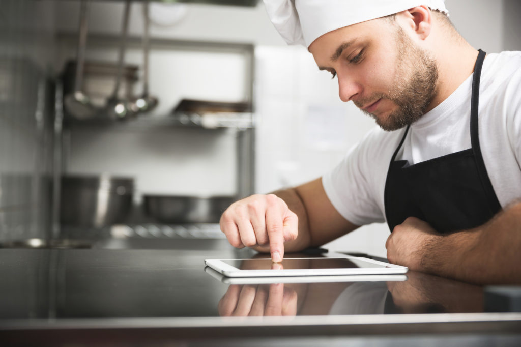 Male cook wearing apron scrolling through ipad