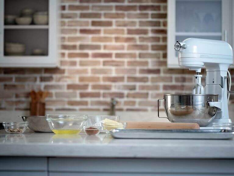 Individual glass bowls containing oil, butter, flour, sugar, and other ingredients arranged on a countertop for almond tuile preparation.