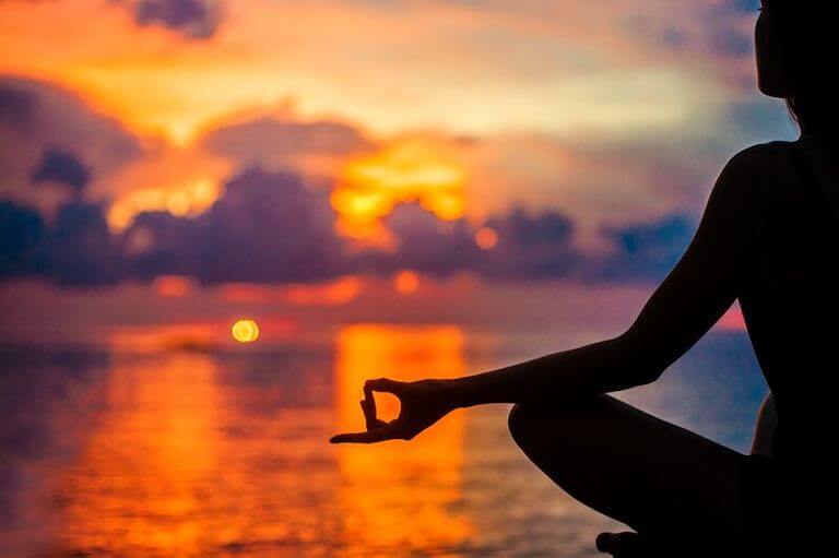 Image shows a silhouette of a seated person practicing meditation in front of a sunset.