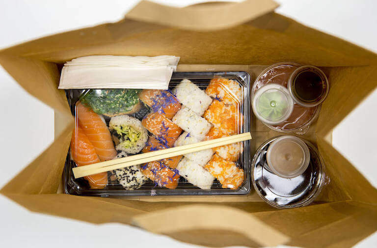 A view inside a to-go bag containing well-presented sushi and separately packaged sides.