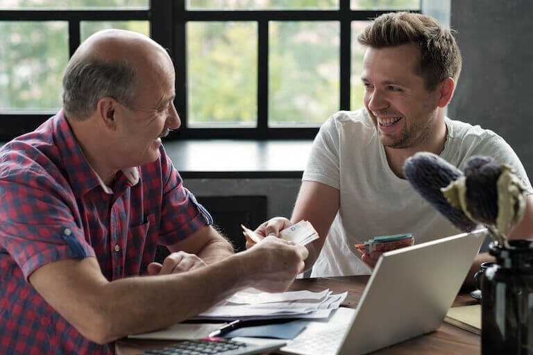 Two people exchanging money as they sit at a table with a laptop