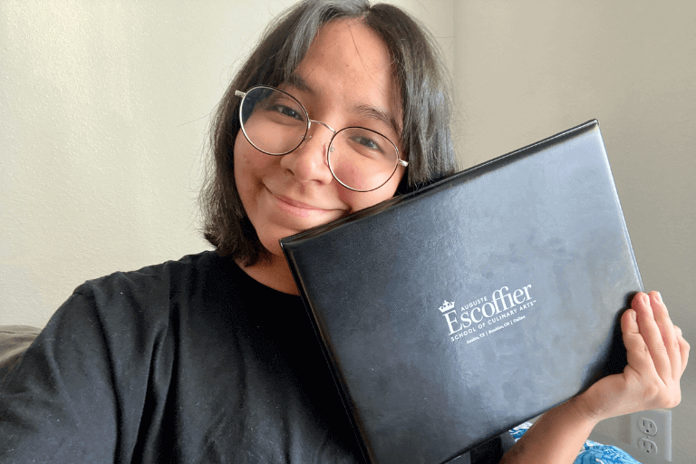 A selfie of a smiling Estefania Colamarco holding her diploma from Escoffier.