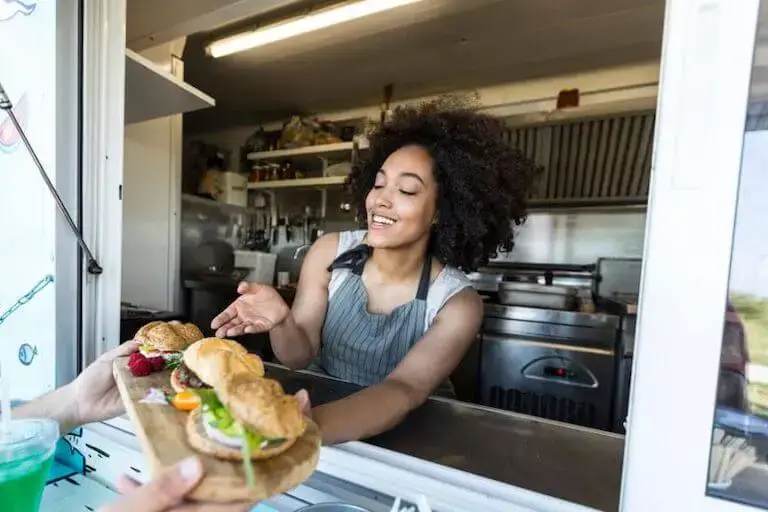 Woman handing sandwiches out of a food truck window to a customer